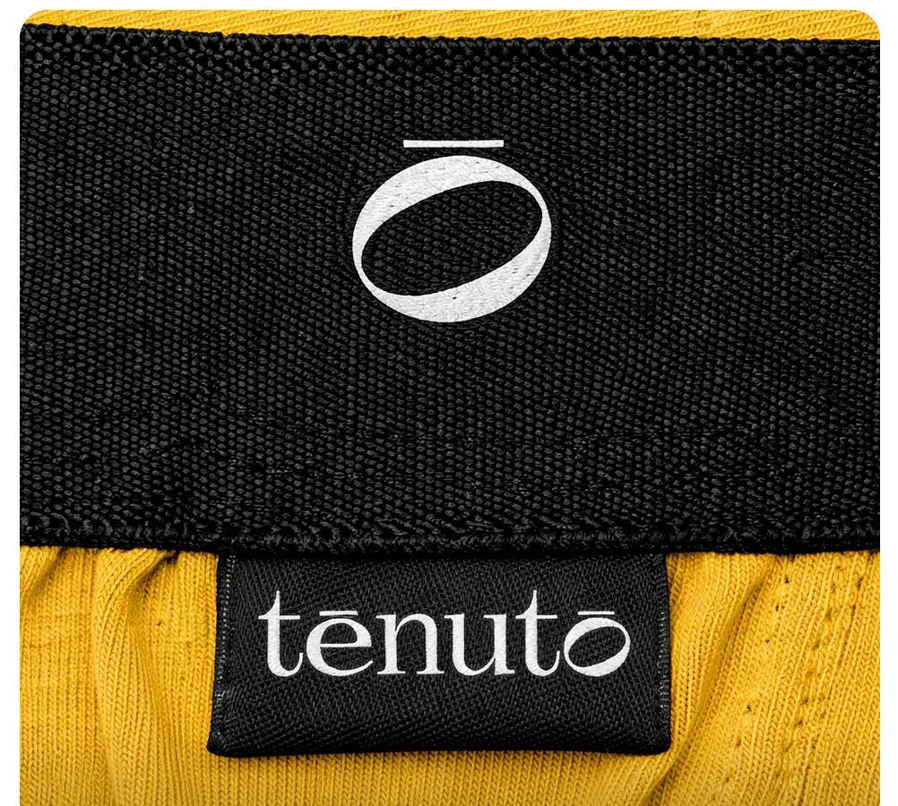 Black waistband with a white embroidered isotype and a woven label with the white wordmark, on yellow fabric